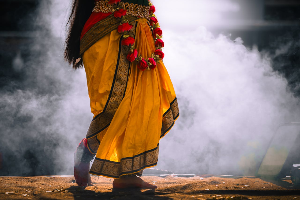 A woman performs a traditional Indian dance, wearing a vibrant yellow saree and red flower garland.